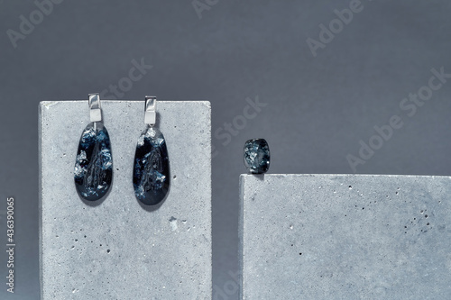 Handmade set of a ring and dangle teardrop earrings made of dark blue epoxy resin with silver foil inside on concrete elements isolated over gray background photo