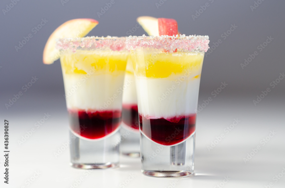 Three layered shot drink based on liqueur, cream and apple peach juice, decorated with colored sugar and a slice of apple Three layered shot drink based on liqueur, cream and apple peach juice, decorated with colored sugar and a slice of apple