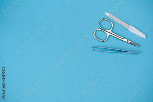 Nail scissors, tweezers and nail file are on the right side on blue background, copy space for any text