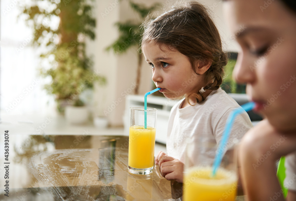 Beautiful baby girl drinking orange juice. Blurry boy on the foreground Beautiful baby girl drinking orange juice. Blurry boy on the foreground
