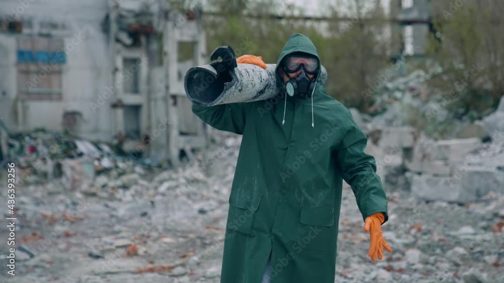 Worker in protective suit in radiation zone. Builder in safety uniform and gas mask is carrying pipe in destroyed place. Chemical attack. Worker in protective suit in radiation zone. Builder in safety uniform and gas mask is carrying pipe in destroyed place. Chemical attack.