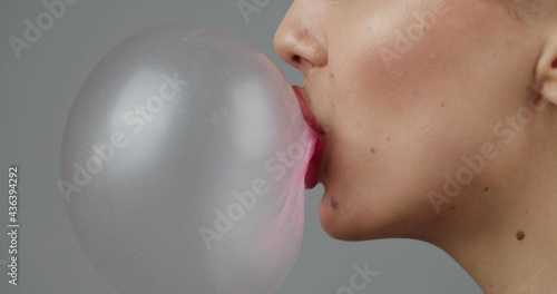 Young woman blowing a bubble with gum on grey background, closeup