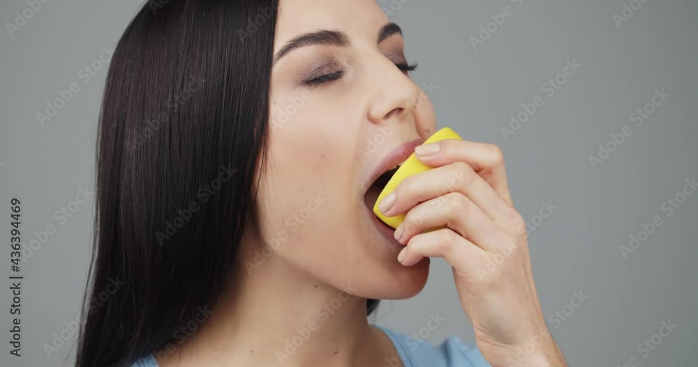 Beautiful young woman eating fresh lemon on grey background Beautiful young woman eating fresh lemon on grey background