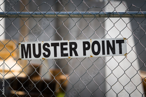 Muster point sign posted on a construction site chain link fence. Fire code and safety at the workplace background