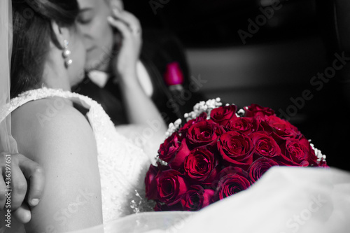 groom and bride cuddling in the car between the wedding ceremony with a bouquet of red roses