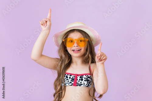 A girl in a swimsuit and sunglasses points her fingers up. On an isolated background.