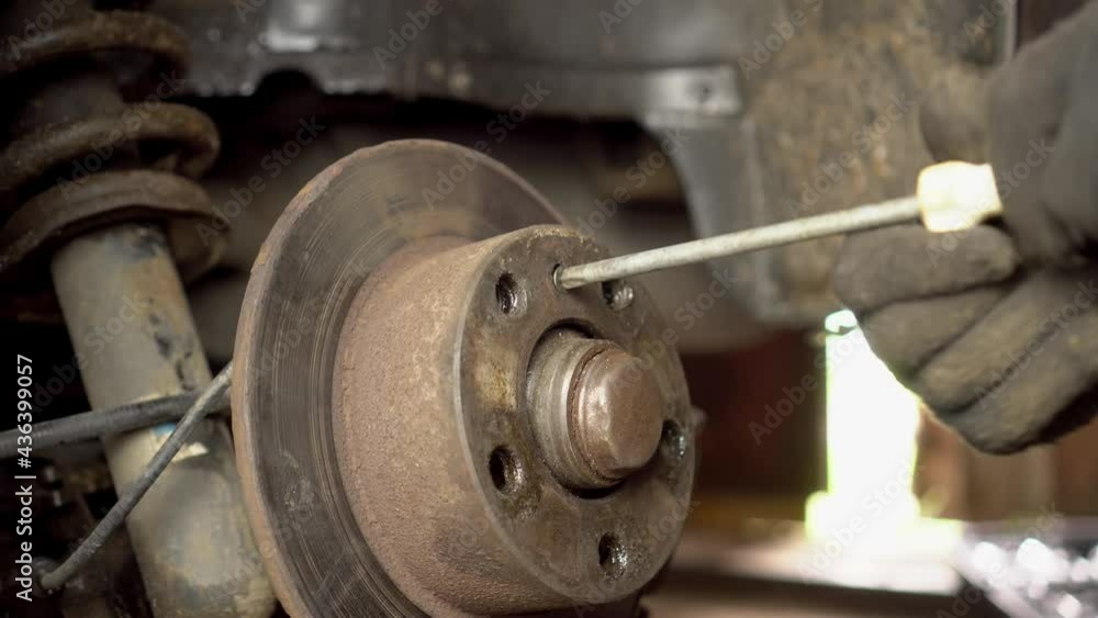 The hands of a master or car mechanic repair the brakes in the car. He unscrews the brake disc with a screwdriver to replace the bearing. Inspection of the car suspension. The hands of a master or car mechanic repair the brakes in the car. He unscrews the brake disc with a screwdriver to replace the bearing. Inspection of the car suspension.