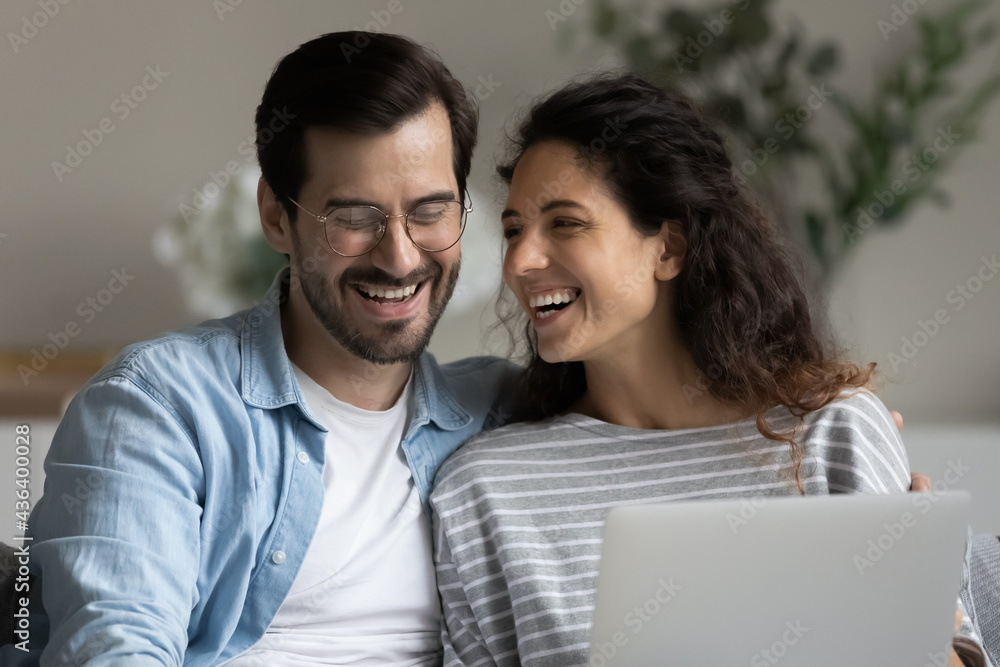 Close up of smiling young multiracial couple laugh using modern computer gather at home together. Happy multiethnic man and woman have fun browsing internet on laptop. Technology concept. Close up of smiling young multiracial couple laugh using modern computer gather at home together. Happy multiethnic man and woman have fun browsing internet on laptop. Technology concept.