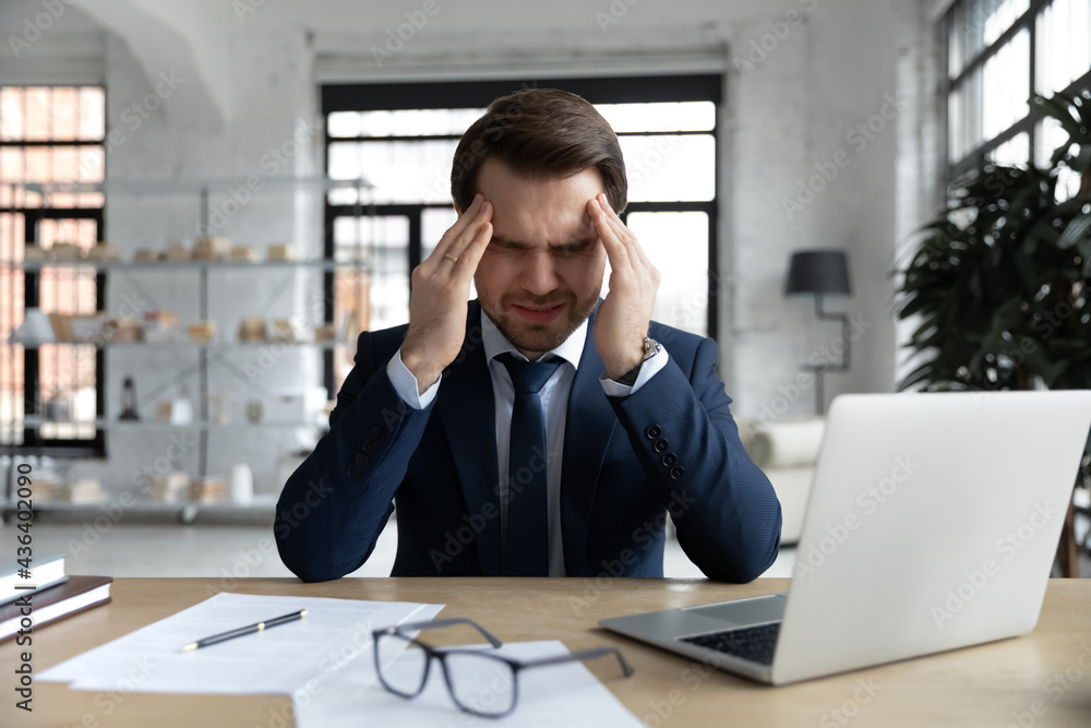 Stressed tired businessman suffering from headache, chronic migraine at workplace, feeling strong pain, holding head with closed eyes. Business professional going through fatigue and nervous breakdown Stressed tired businessman suffering from headache, chronic migraine at workplace, feeling strong pain, holding head with closed eyes. Business professional going through fatigue and nervous breakdown