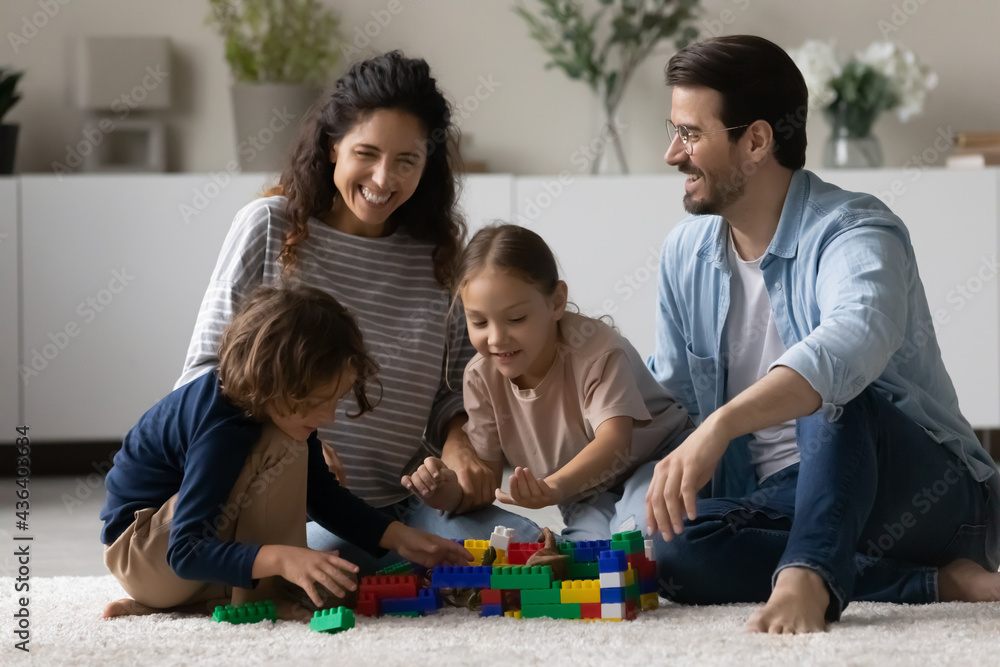 Overjoyed multiethnic parents sit on floor play toys with little biracial kids together. Happy multiracial young family with small ethnic children have fun engaged in playful game activity at home. Overjoyed multiethnic parents sit on floor play toys with little biracial kids together. Happy multiracial young family with small ethnic children have fun engaged in playful game activity at home.