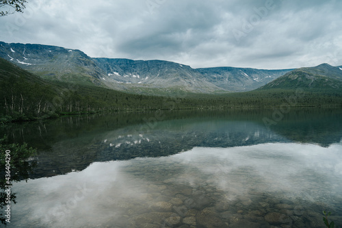 Mountain ranges are reflected in the mirror surface of the lake in cloudy weather in polar summer. Mountain landscape in Kola Peninsula, Arctic