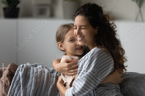 Smiling young Latino mother hug cuddle small biracial daughter show love care. Happy Hispanic mom embrace little ethnic girl child, relax enjoy family weekend at home together. Motherhood concept.