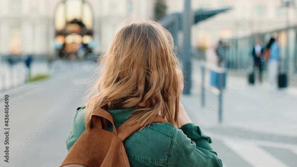 Back view of young Caucasian woman with backpack walking on street at bus stop travelling speaking on smartphone. Female tourist in mask calling on cellphone outdoors, Travel, close up concept Back view of young Caucasian woman with backpack walking on street at bus stop travelling speaking on smartphone. Female tourist in mask calling on cellphone outdoors, Travel, close up concept