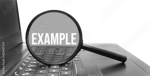 A concept image of a magnifying glass isolated white background with a word EXAMPLE zoom inside the glass on laptop keyboard photo