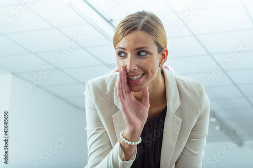 Middle-aged businesswoman bending to gossip with the viewer photo