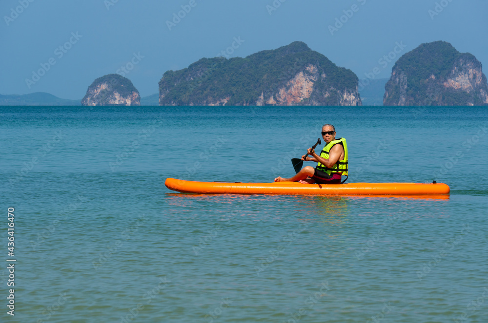 senior asian man playing paddle board in blue sea during summer vacation