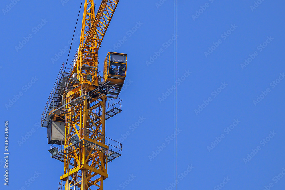 The top part of a working construction crane on a blue sky background The top part of a working construction crane on a blue sky background