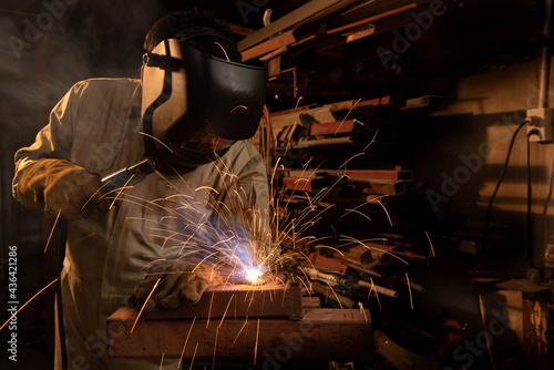 A welder is welding steel in an industrial factory. The welder wears protective clothing to work in the workplace.