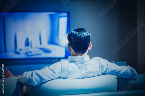 Back rear view man sitting on a sofa watching tv or streaming with smart tv evening and Room at home leisure, technology, relax, at home,Home relaxation concept and happiness