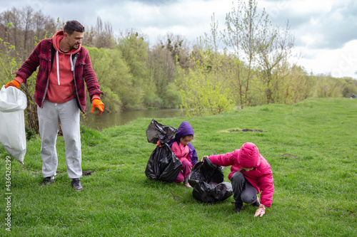 Dad and his little daughters are cleaning the environment in the forest.