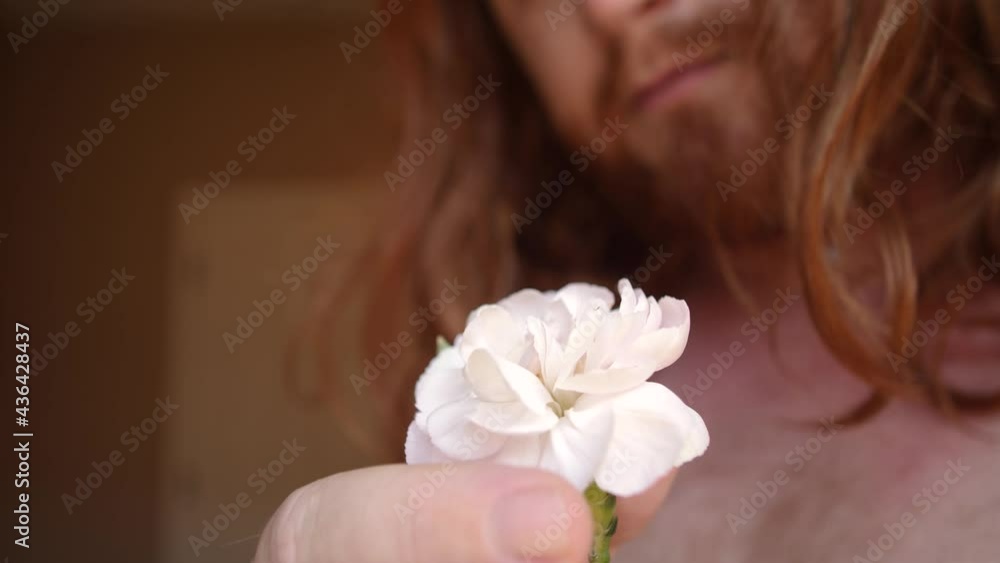Red haired Man softly touching the pedals of a white and pink flower. Red haired Man softly touching the pedals of a white and pink flower.