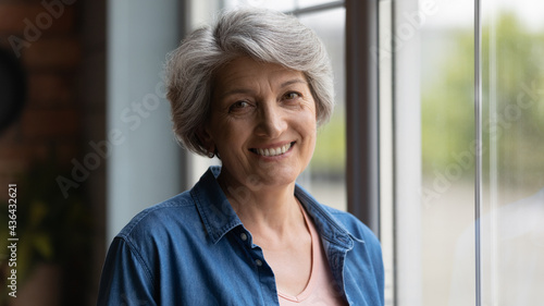 Cuadro en lienzo Elderly 60s woman with short haircut smile look at camera enjoy peaceful midlife retired life standing near window posing alone indoors