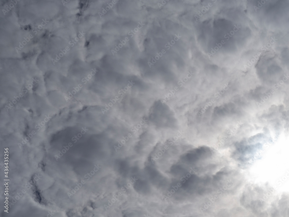 Solid gray-white Cumulus Clouds through which the Sun breaks through. Cloudy natural background