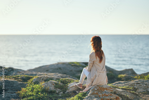 travel woman in sweater sits on a high stone near the sea in the mountains back view