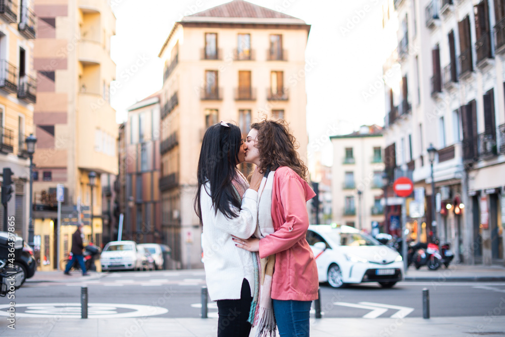 two girls, one with brown hair and the other with curly hair kissing on the mouth in the city. lesbian concept. tourism concept 