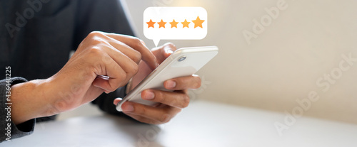 close up on man hand press on smartphone screen with gold five star rating feedback icon and press level excellent rank for giving best score point to review the service , technology business photo