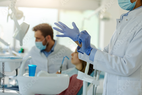 A photo of a female dentist putting on gloves while preparing for a dental examination.