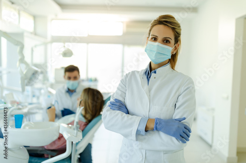 Dentist female with crossed arms wearing white coat posing and looking at camera.