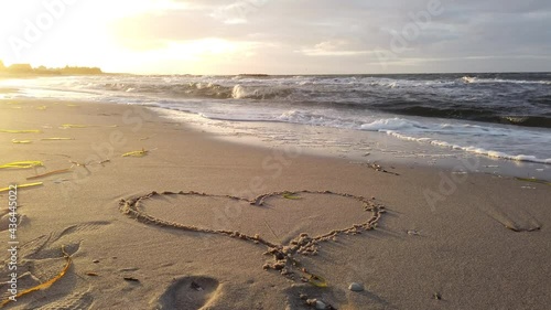 Heart drawn into sand at beach is washed away by rushing surf at sunset, 4k video footage