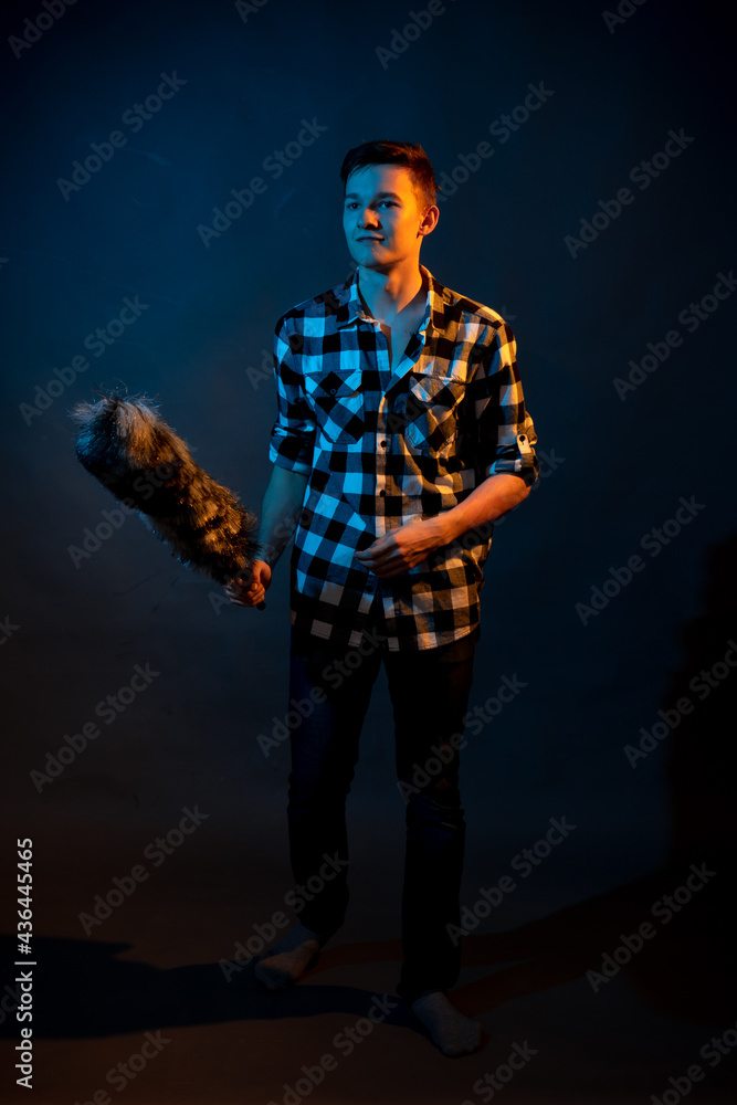 A guy in a plaid shirt with a dust brush on a dark background illuminated by blue and yellow light