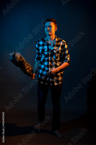 A guy in a plaid shirt with a dust brush on a dark background illuminated by blue and yellow light