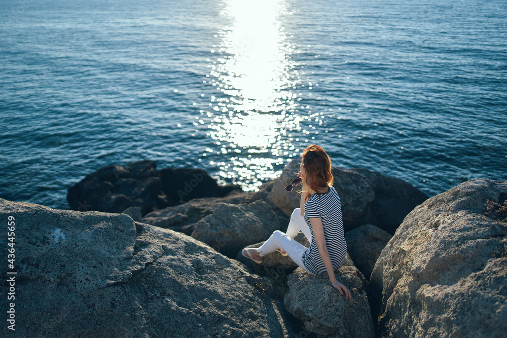 woman traveler sitting on stones near the sea landscape beach sunset clear water