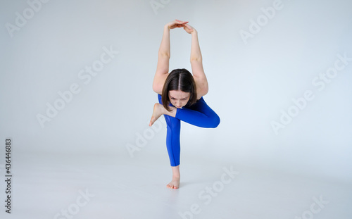 Portrait of sporty woman doing Kapotasana or standing Pigeon Pose. Attractive young woman training yoga on white background isolated on cyclorama. photo