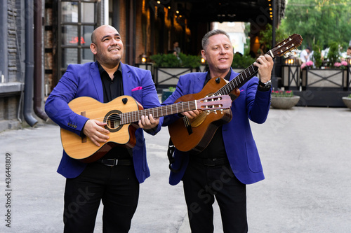 Caucasian and latin musicians play acoustic guitars in the street