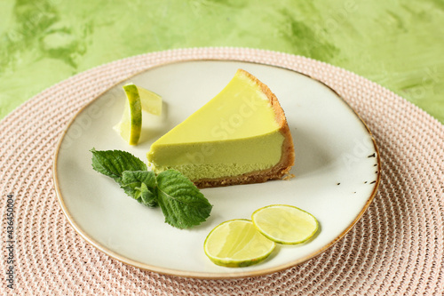 Slice of lemon cheesecake on a round plate. A piece of delicious cake served with mint and lime slices