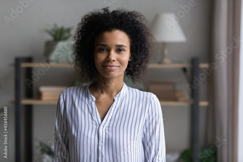 Profile picture of smiling young African American woman posing in own living room at home. Headshot portrait of happy mixed race female renter or tenant in new apartment or house. Diversity concept.