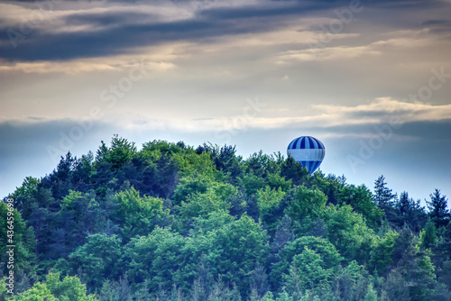 scenic view of a hot-air balloon behind the woodland on a hill