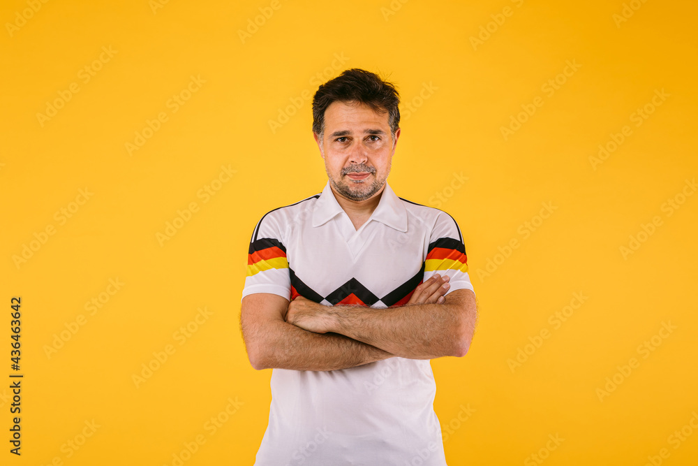 Soccer fan wearing a white t-shirt with black, red and yellow stripes, poses with crossed arms Soccer fan wearing a white t-shirt with black, red and yellow stripes, poses with crossed arms