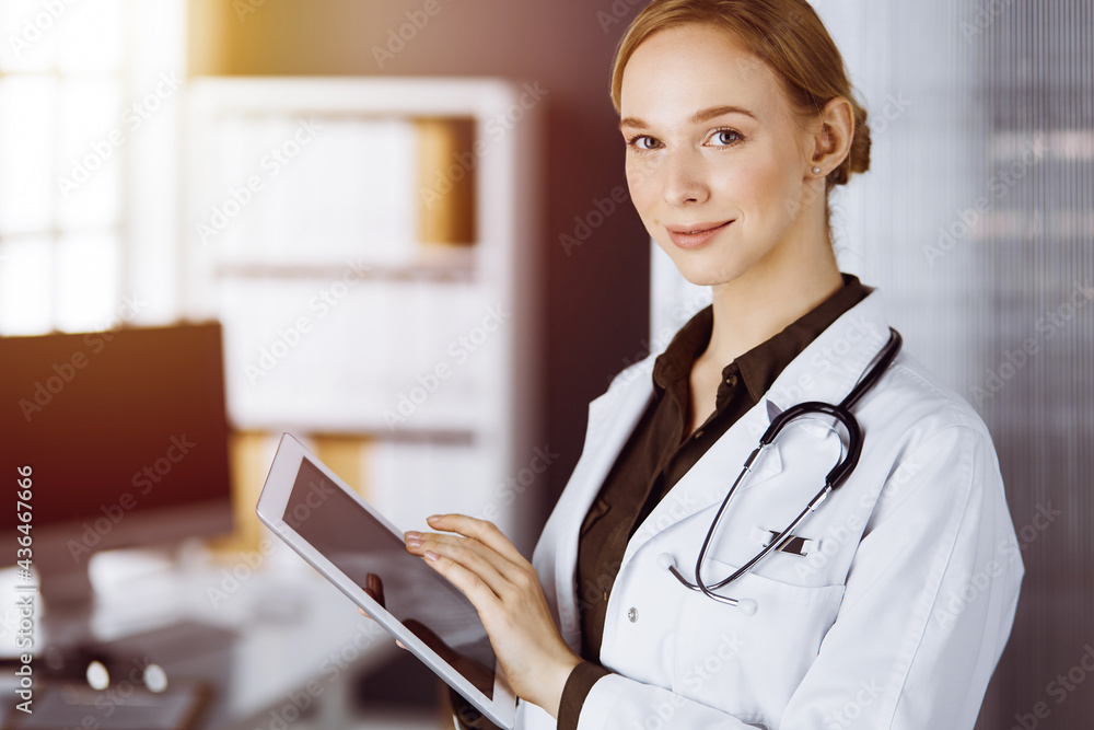 Cheerful smiling female doctor using clipboard in clinic. Portrait of friendly physician woman at work. Medical service in hospital. Medicine concept Cheerful smiling female doctor using clipboard in clinic. Portrait of friendly physician woman at work. Medical service in hospital. Medicine concept