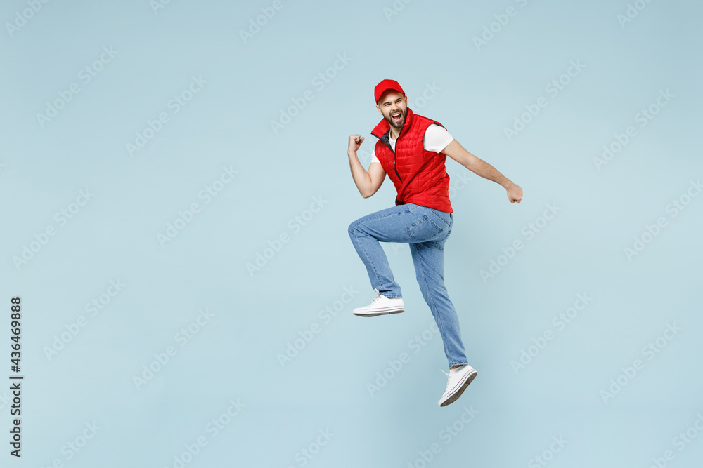 Full size body length side view delivery guy employee man in red cap white T-shirt vest uniform work dealer courier jump run go walk isolated on pastel blue color background studio. Service concept Full size body length side view delivery guy employee man in red cap white T-shirt vest uniform work dealer courier jump run go walk isolated on pastel blue color background studio. Service concept