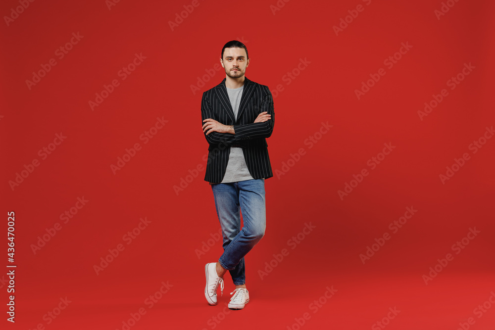 Full length young serious businessman latin man 20s with long hair ponytail wearing black striped jacket grey shirt look camera hold hands crossed folded isolated on red background studio portrait Full length young serious businessman latin man 20s with long hair ponytail wearing black striped jacket grey shirt look camera hold hands crossed folded isolated on red background studio portrait