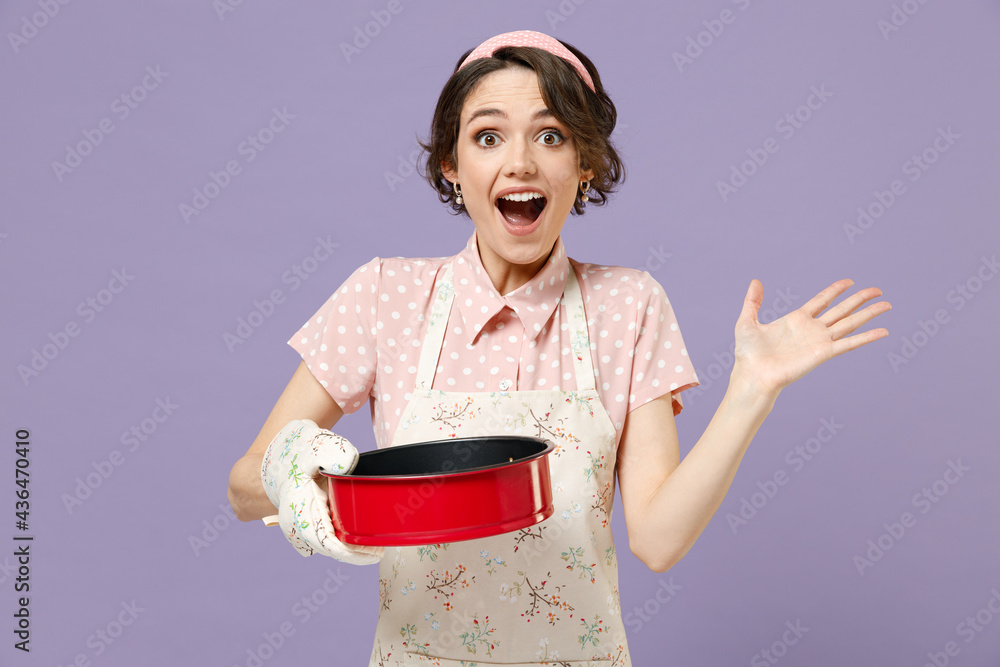 Φωτογραφία Young surprised housewife housekeeper chef cook baker woman in pink apron holding red non-stick baking form for pie cake spread hands isolated on pastel violet background Cooking food process concept