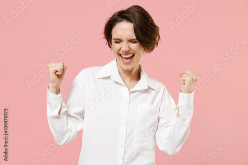 Young overjoyed successful employee business woman corporate lawyer 20s in classic formal white shirt work in office do winner gesture clench fist isolated on pastel pink background studio portrait. photo