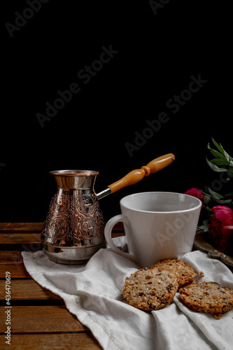 turk with coffee, black coffee cup, red flowers, cookies, lemon, wooden table, black background © Anastasia Bondarenko