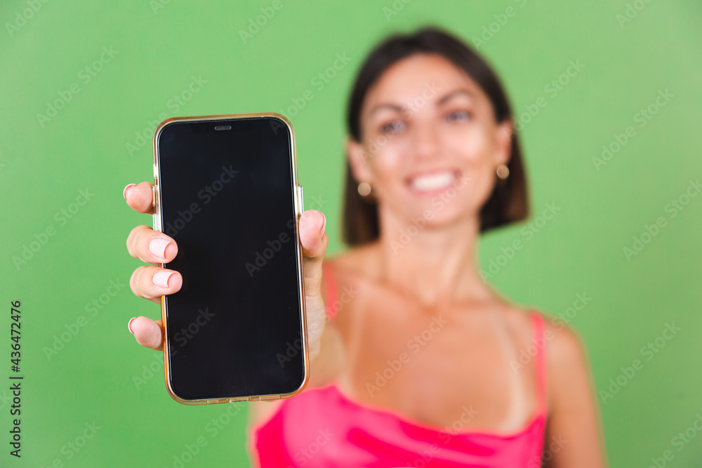 Stylish woman in pink silk dress isolated on green background happy excited point on black empty mobile phone screen Stylish woman in pink silk dress isolated on green background happy excited point on black empty mobile phone screen