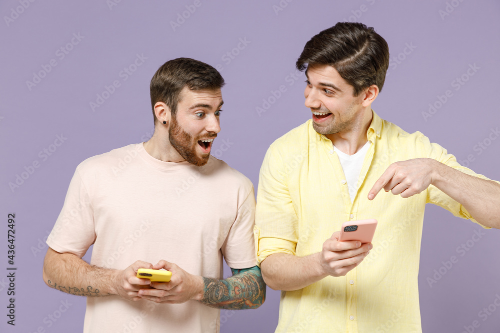 Young smiling cool happy men friends together in casual t-shirt tattoo translate fun hold mobile cell phone chat online point index finger show isolated on purple background People lifestyle concept Young smiling cool happy men friends together in casual t-shirt tattoo translate fun hold mobile cell phone chat online point index finger show isolated on purple background People lifestyle concept
